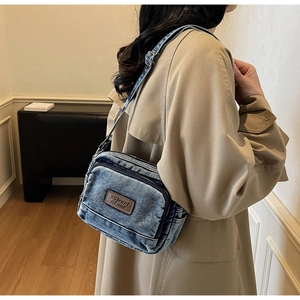 Détail d'un sac bandoulière en denim délavé bleu avec un écusson logo en cuir marron