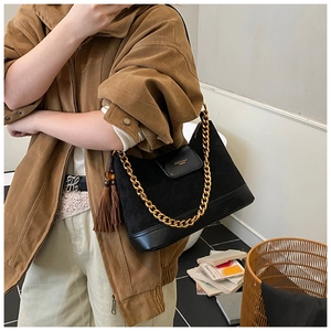 Detail of black suede shoulder bag featuring a chunky gold chain and tassel charm
