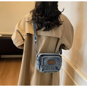 Détail d'un sac bandoulière en denim délavé avec un patch logo en cuir marron vintage