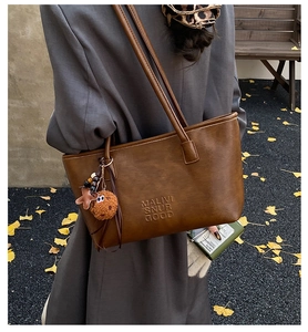 Détail d'un grand sac fourre-tout marron avec gaufrage de lettres et pendentif en peluche