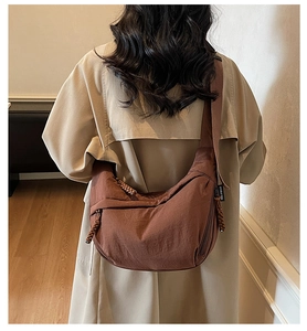 Detail of a brown crescent canvas bag with textured folds and braided zipper pull