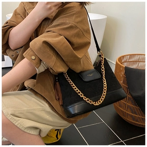 Detail of black suede shoulder bag featuring a gold chunky chain and quilted leather base