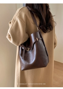 Sac seau marron foncé en cuir grainé avec boucle dorée porté par un mannequin