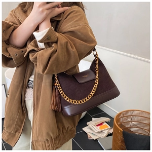 Detail of dark brown suede shoulder bag with gold chain strap and elegant tassel
