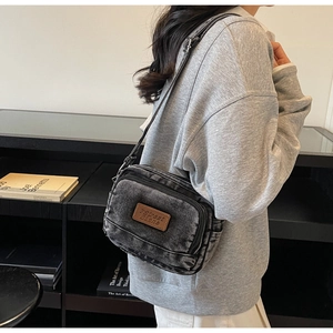 Détail du sac bandoulière en denim lavé avec sangle réglable et étiquette logo en cuir
