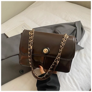 Detailed macro view of dark coffee glossy leather handbag with gold chain and round buckle