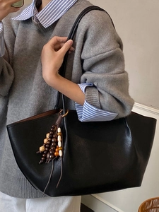 Large black matte leather tote bag with vintage wooden beads on a stylish model