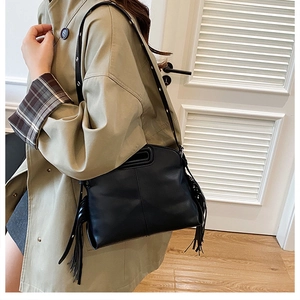 Détail du sac bandoulière noir avec franges et poignée évidée porté sur un trench-coat