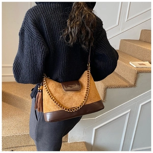 Detail of brown suede crossbody bag featuring gold chain strap and elegant tassel pendant