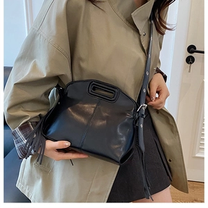 Détail d'un sac à main noir avec poignée découpée et longs glands à franges