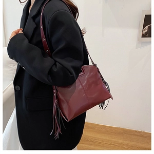 Vue détaillée du sac à bandoulière en cuir bordeaux avec pompon et sangle ajustable