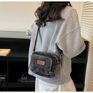 Détail d'un sac bandoulière en denim délavé foncé avec plusieurs poches et un patch