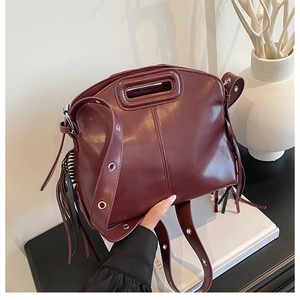 Détail du sac à bandoulière bordeaux avec pompon et large sangle à œillets argentés
