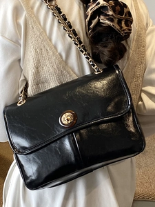 Minimalist black leather crossbody bag with gold chain strap and circular lock closure