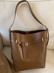 Sac seau chic en cuir marron caramel avec boucle dorée posé sur un canapé beige