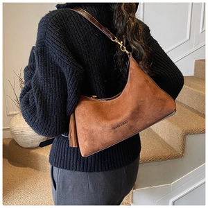 Detail of retro brown suede crescent bag with fringe and glossy dark leather strap