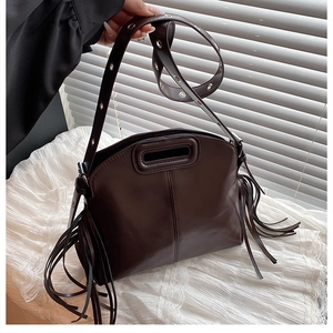 Détail d'un sac bandoulière marron avec glands latéraux et œillets argentés sur la sangle
