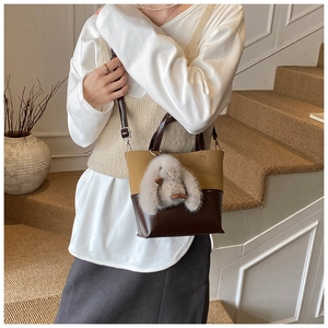 Detail of a vintage-style bucket bag with a plush bunny charm and contrasting leather texture