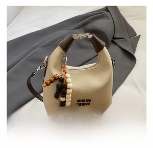Detail of beige canvas handbag with leather trim, metal clasp, and beaded tassel charm