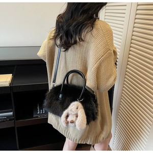 Détail d'un sac cabas en peluche noire avec un lapin beige sur un pull en maille beige