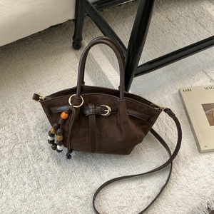 Détail d'un sac cabas en daim marron foncé avec boucle métallique et breloque perlée