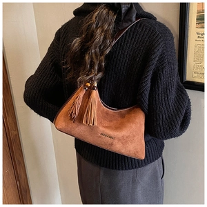 Detail of a brown suede half-moon underarm bag with vintage tassel and embossed logo