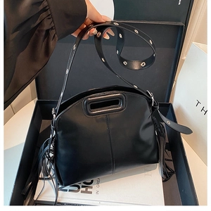 Détail d'un sac à main trapèze en cuir noir avec des franges latérales dans un coffret cadeau