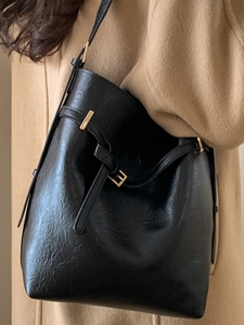 Sac seau chic en cuir noir avec boucles dorées porté sur un manteau en laine