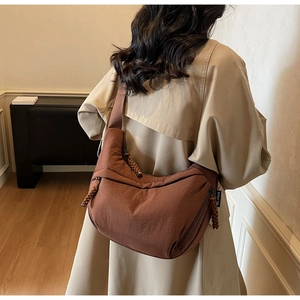 Brown nylon crescent bag worn crossbody over a beige trench coat showing size and fit
