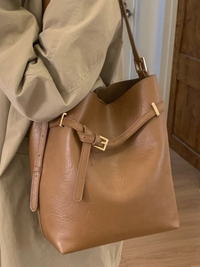 Sac seau élégant en cuir marron avec détails dorés porté avec un trench-coat beige