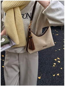 Detail of beige hobo shoulder bag with brown leather trim and tassel on ginkgo leaf ground
