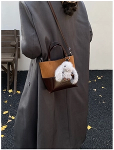 Detail view of vintage contrast leather bucket bag with a plush bunny charm outdoors