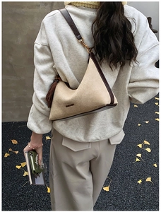 Detail of beige suede hobo bag with dark brown trim and golden buckle on shoulder