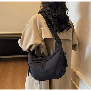 Detail view of a large black canvas dumpling bag with an adjustable wide strap on a model