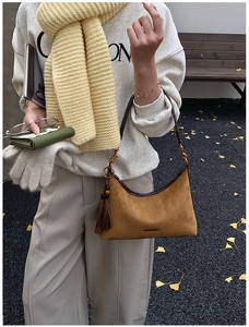 Brown suede hobo bag with tassel detail and brand logo shown in an autumn street setting