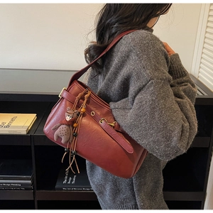 Détail du sac Boston bordeaux avec boucle en métal, longues franges et pendentif ours peluche