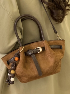 Sac à main en daim marron avec sangles en cuir et breloques en bois sur manteau vert