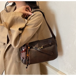 Détail d'un sac à bandoulière vintage marron avec œillets et pendentif ours