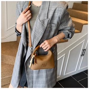 Brown leather handbag with wooden bead charm detail held by model in plaid blazer