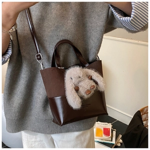 Detail showing mixed texture dark brown bucket bag with a cute plush rabbit pendant