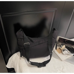 Detail of black crescent crossbody bag with wide strap and plastic buckle on white bedding