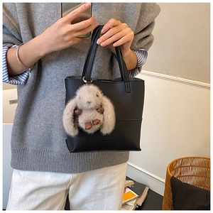 Detail of black litchi texture handbag featuring a cute grey plush rabbit pendant accessory