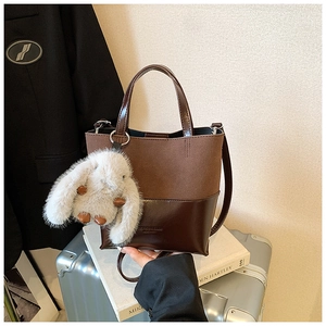 Close-up of vintage brown bucket bag with plush bunny charm on a suitcase setting