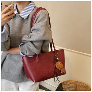 Détail du grand sac cabas bordeaux avec logo embossé et pendentif peluche biscuit