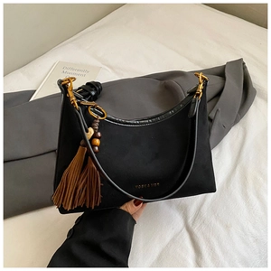 Detail of black suede shoulder bag with golden hardware and ethnic tassel pendant