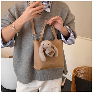 Close-up of khaki pebbled leather bucket bag with cute grey plush rabbit charm