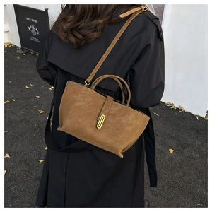 Close-up of brown suede tote bag with golden oval metal clasp on a black coat