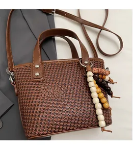 Dettaglio della borsa tote intrecciata marrone con manici in pelle e ciondolo in legno