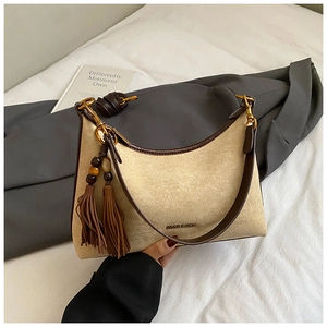Detail of minimalist underarm bag featuring beige suede with brown leather trim and tassels