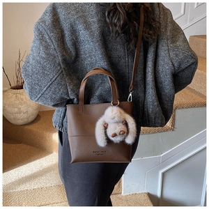 Close-up of brown pebbled leather bucket bag with a cute plush rabbit charm